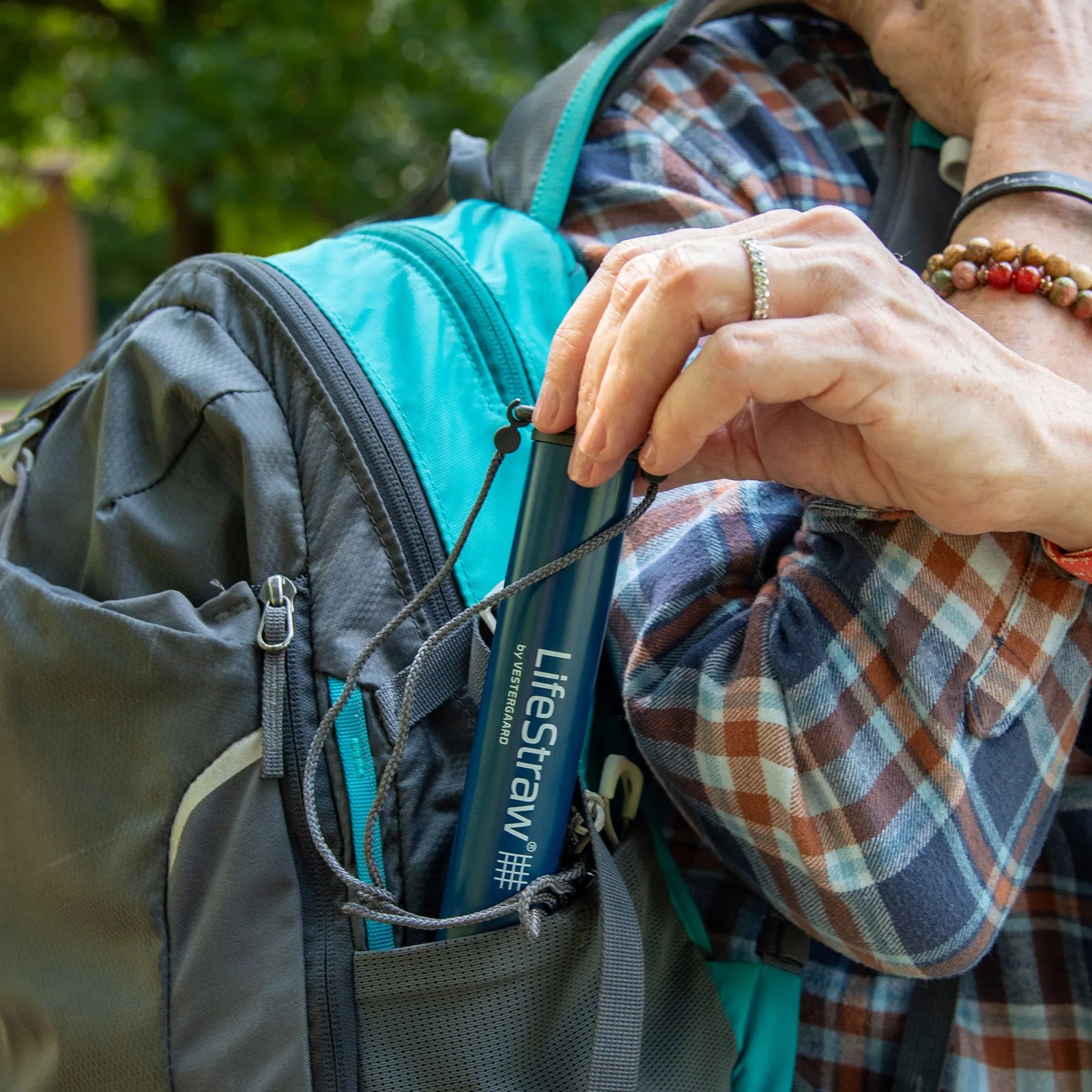 Blue LifeStraw water filter being placed into the side pocket of a gray and turquoise backpack.