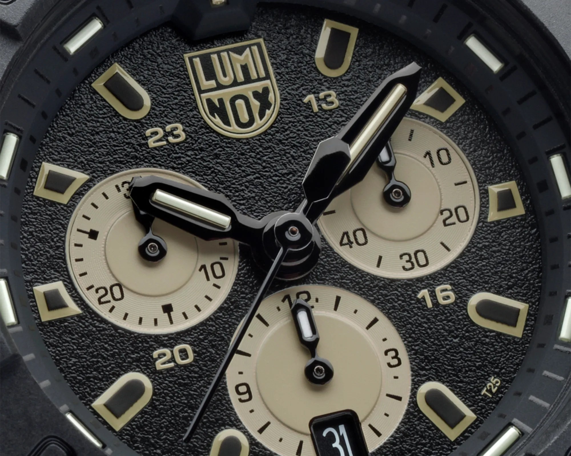 Close-up of a black Luminox watch face with beige subdials, luminous hands, and date display at 6 o'clock.