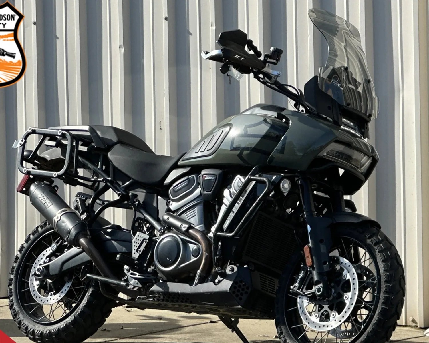 Green and black adventure motorcycle with knobby tires and tall windshield parked in front of a corrugated metal wall.