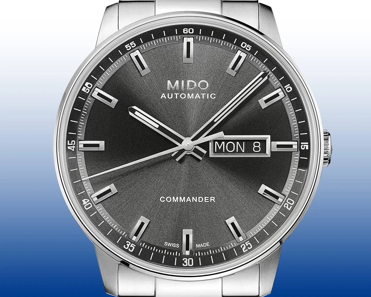 Close-up of a Mido Commander automatic watch with a gray sunburst dial, silver hour markers, and day-date display.