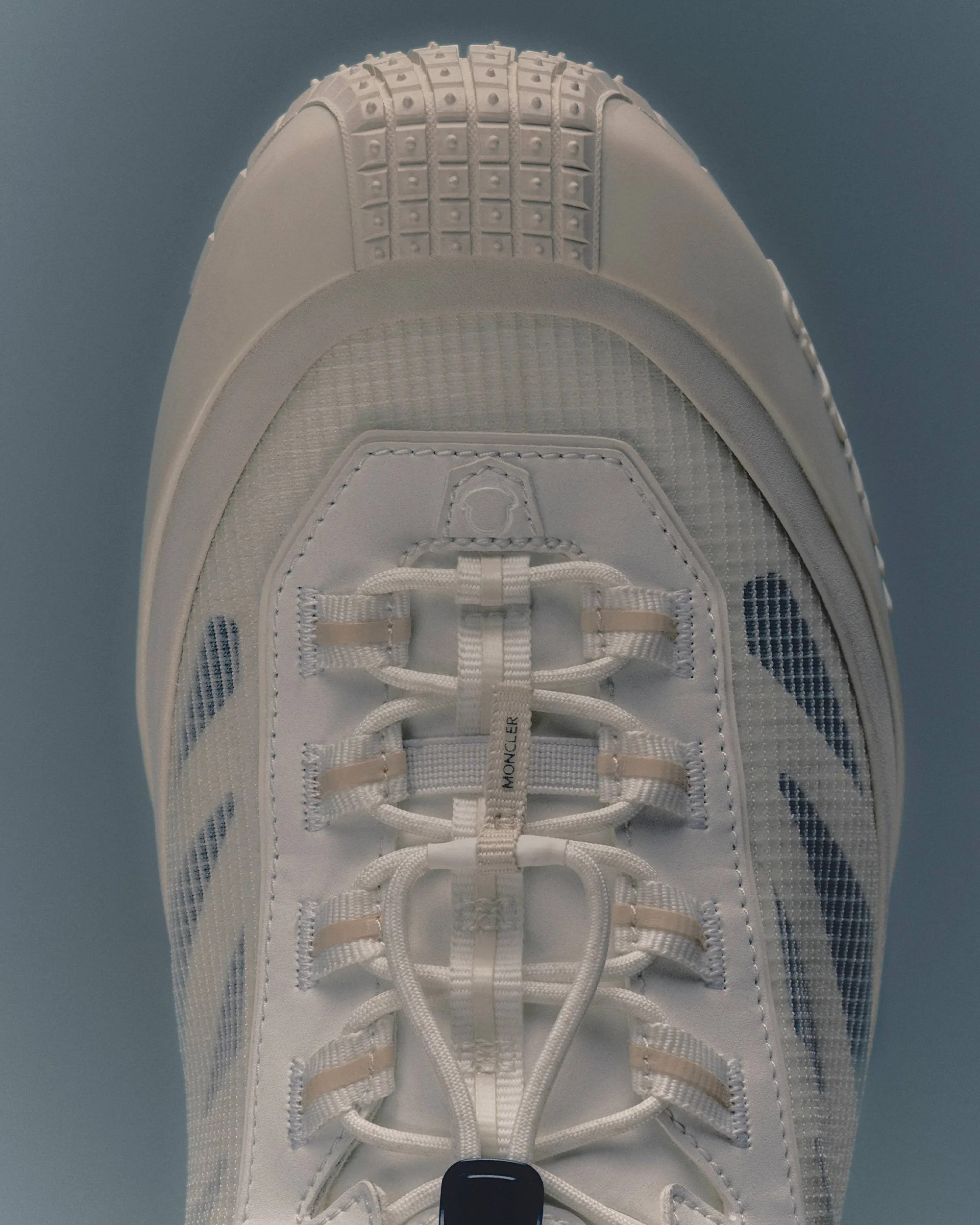 Close-up of a white sneaker toe with detailed lacing and textured rubber sole on a blue background.