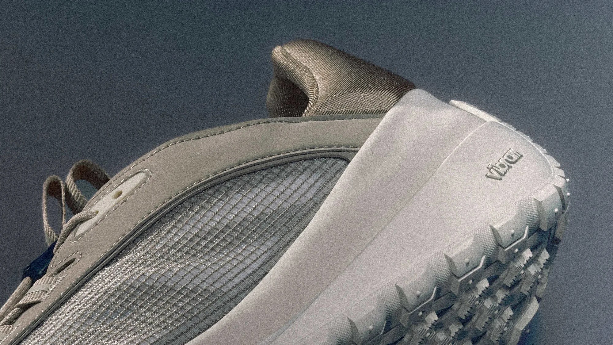 Close-up of a beige and gray sneaker with a textured mesh side panel and a white Vibram sole.