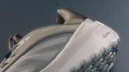 Close-up of a beige and gray sneaker with a textured mesh side panel and a white Vibram sole.