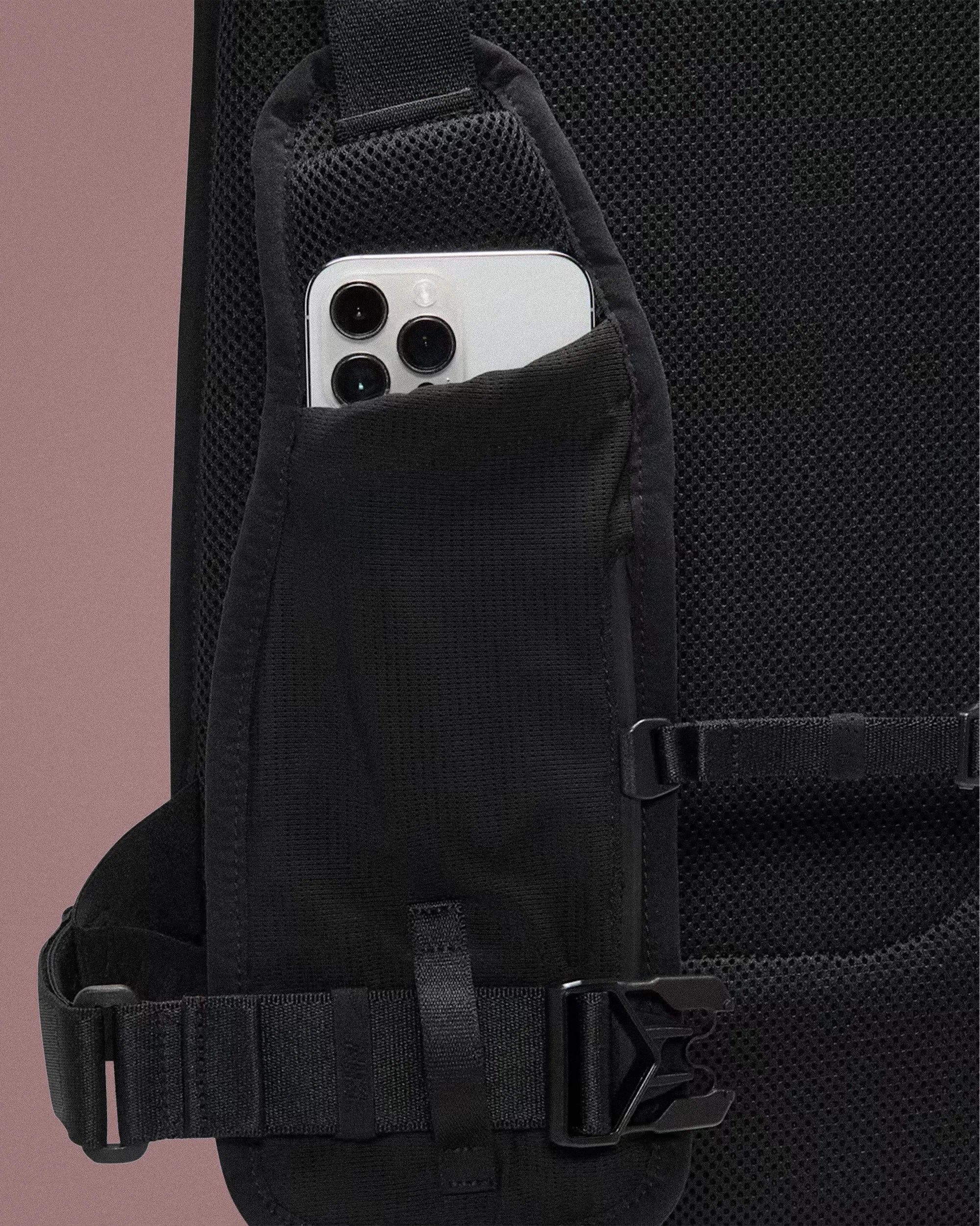 Black mesh backpack strap with a small pocket holding a white smartphone with triple cameras.
