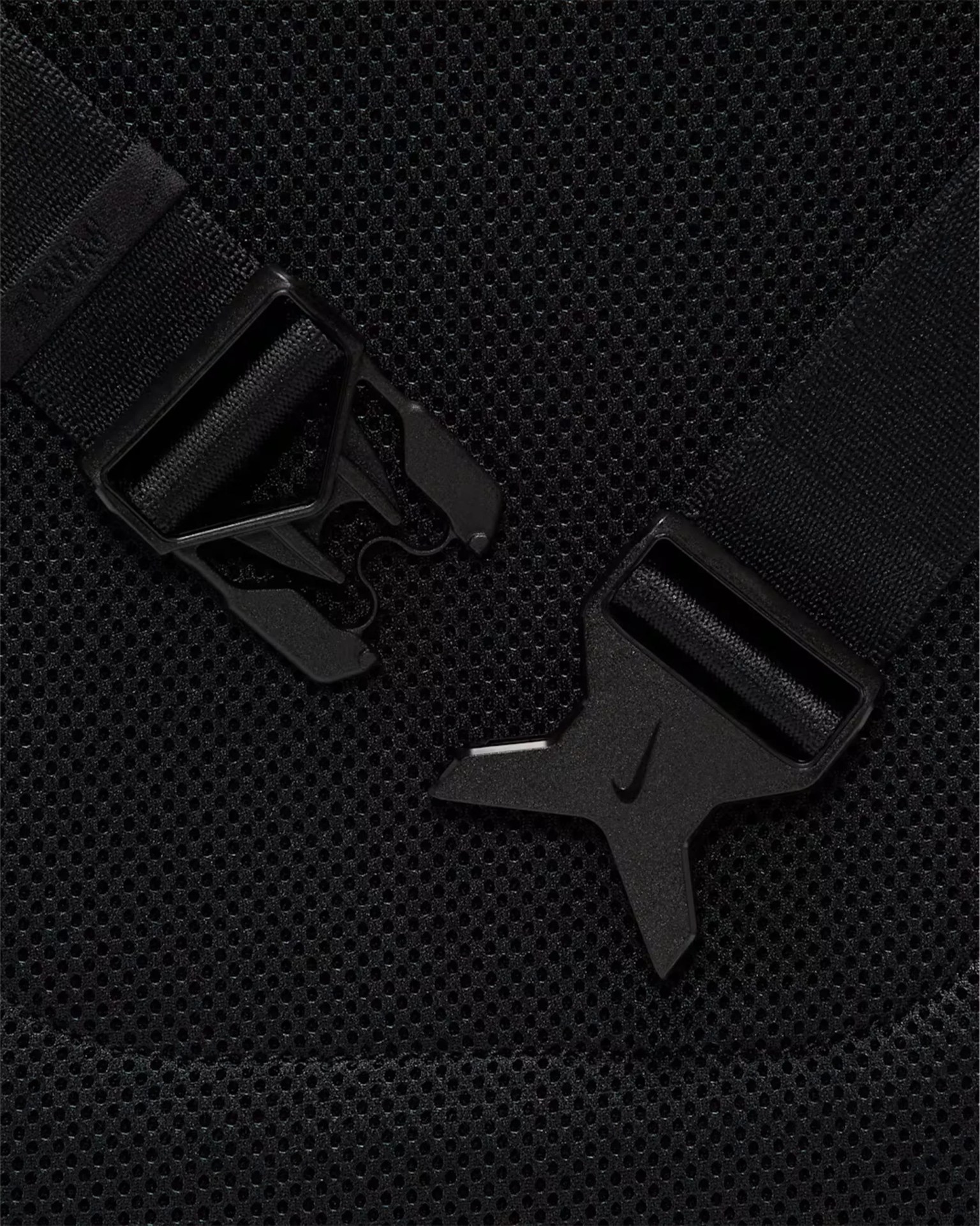 Close-up of a black plastic buckle with a Nike logo on black mesh fabric.