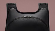 Black padded vest with a front zipper pocket and wide shoulder straps against a brown background.