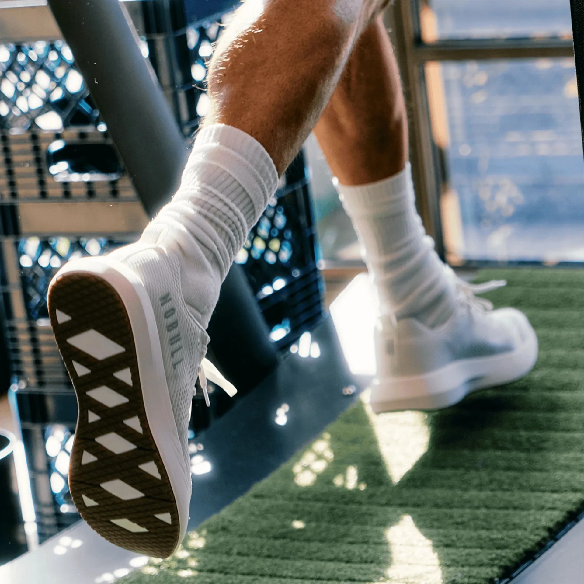 White athletic shoes with patterned brown soles worn with white crew socks on green turf.