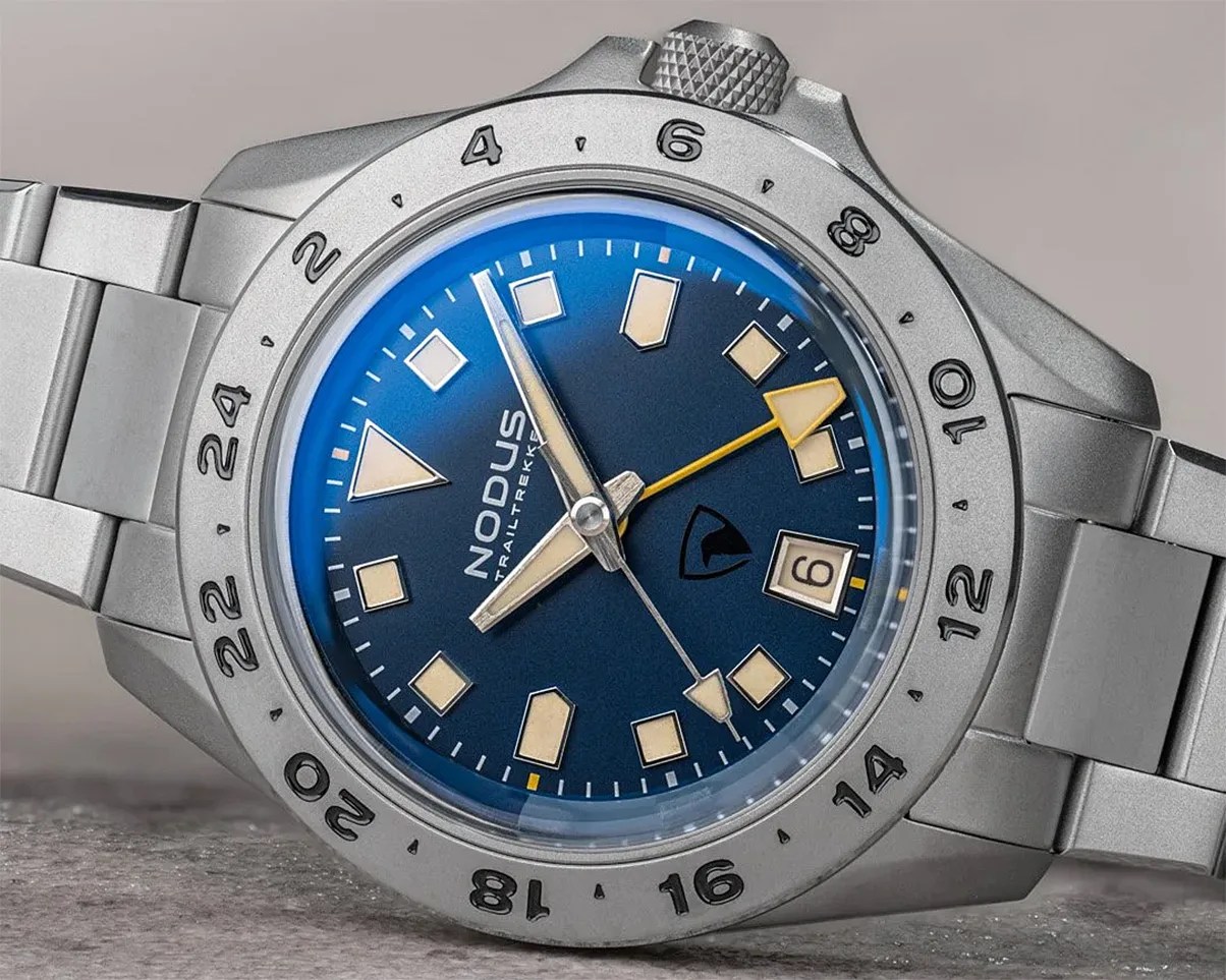 Silver stainless steel wristwatch with blue dial, beige geometric hour markers, yellow GMT hand, and date window.