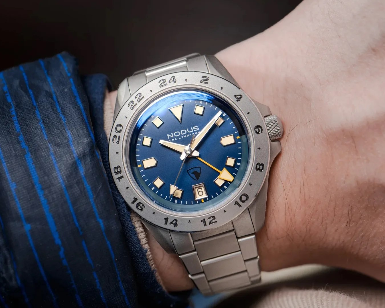Silver metal wristwatch with blue dial, beige hour markers, and orange GMT hand worn on a wrist.