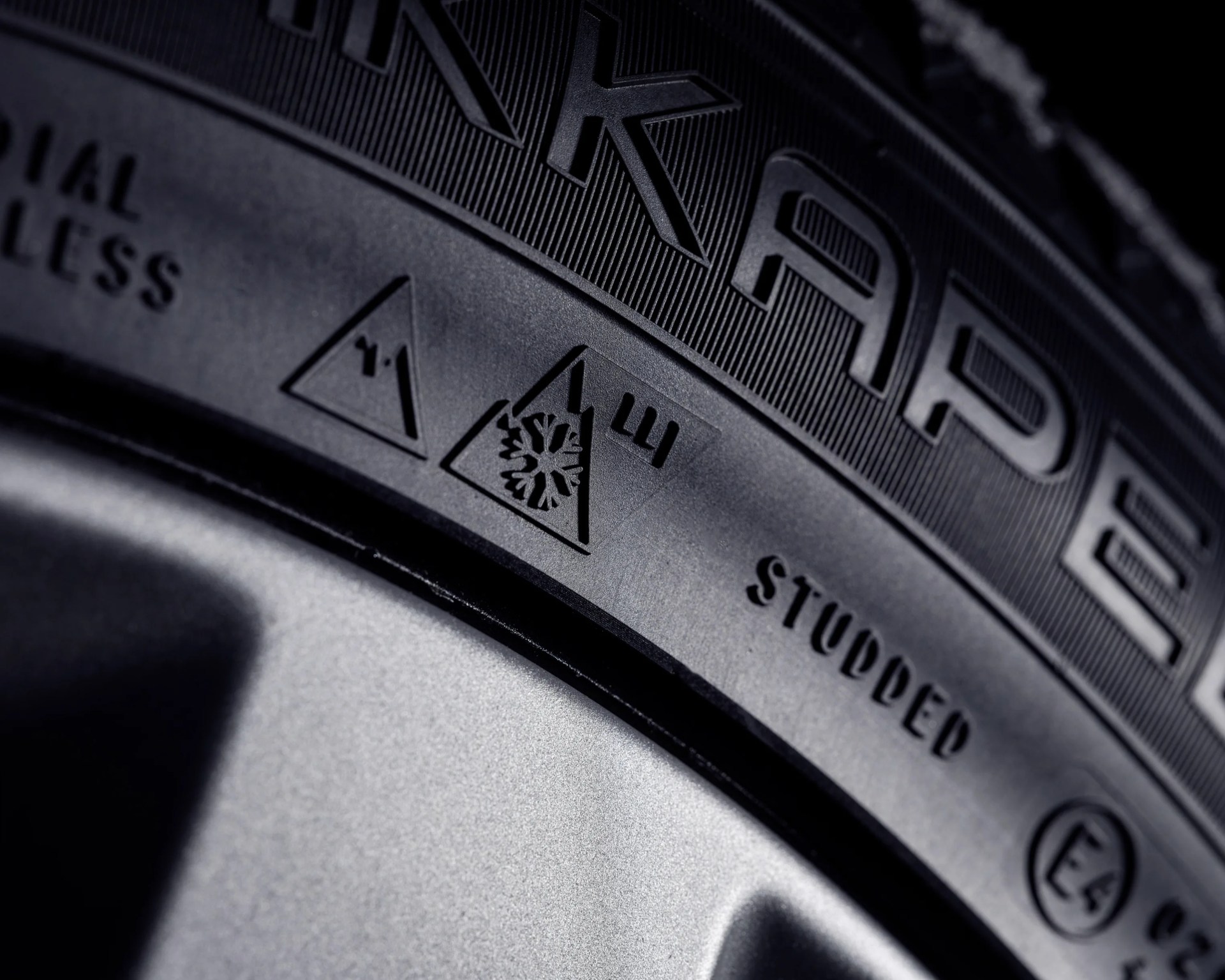 Close-up of a black tire sidewall showing winter tire symbols and the word "STUDDED" near a silver wheel rim.