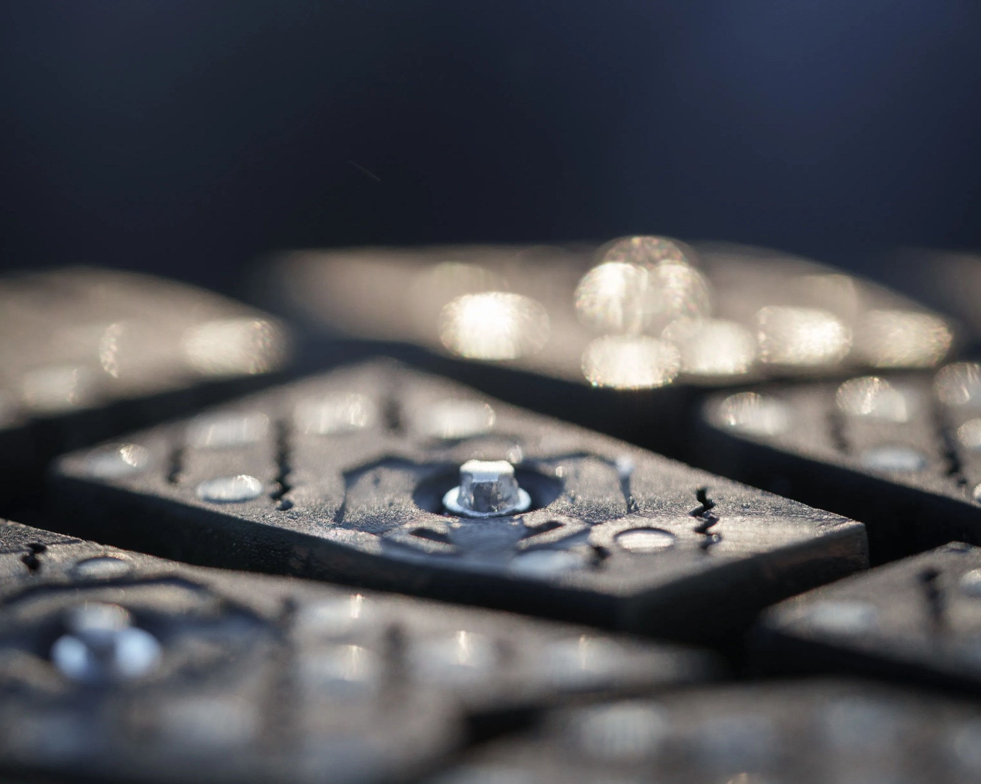 Close-up of a black metal object with a central bolt and engraved patterns, with blurred similar objects in the background.
