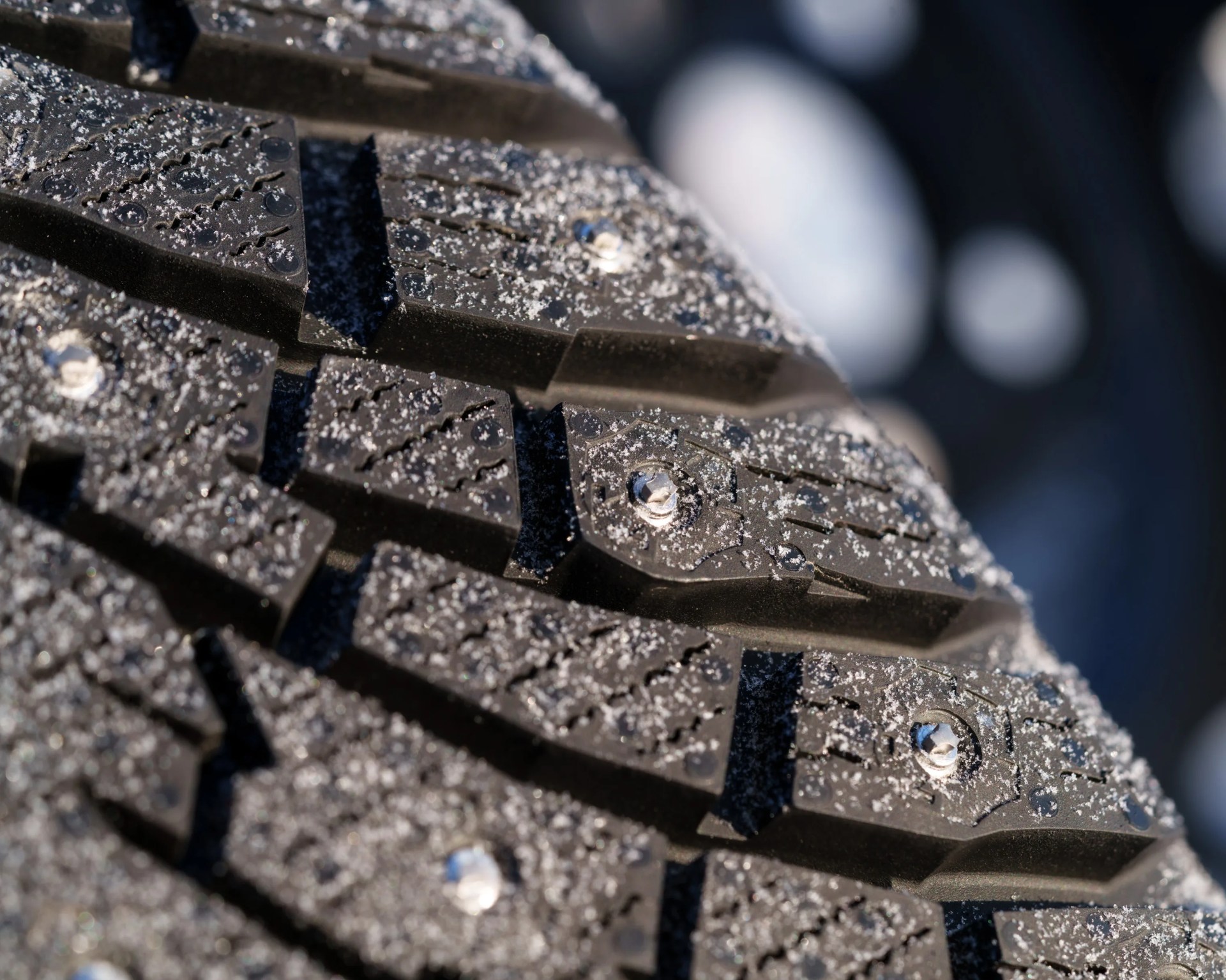 Close-up of a black studded winter tire tread with small ice particles on the surface.