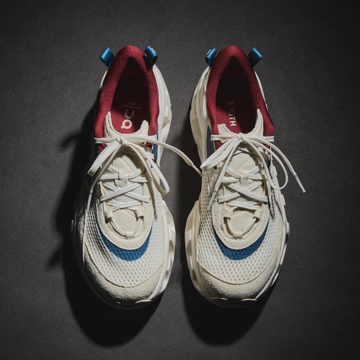 Pair of white mesh and suede sneakers with blue accents and burgundy inner lining on a dark surface.