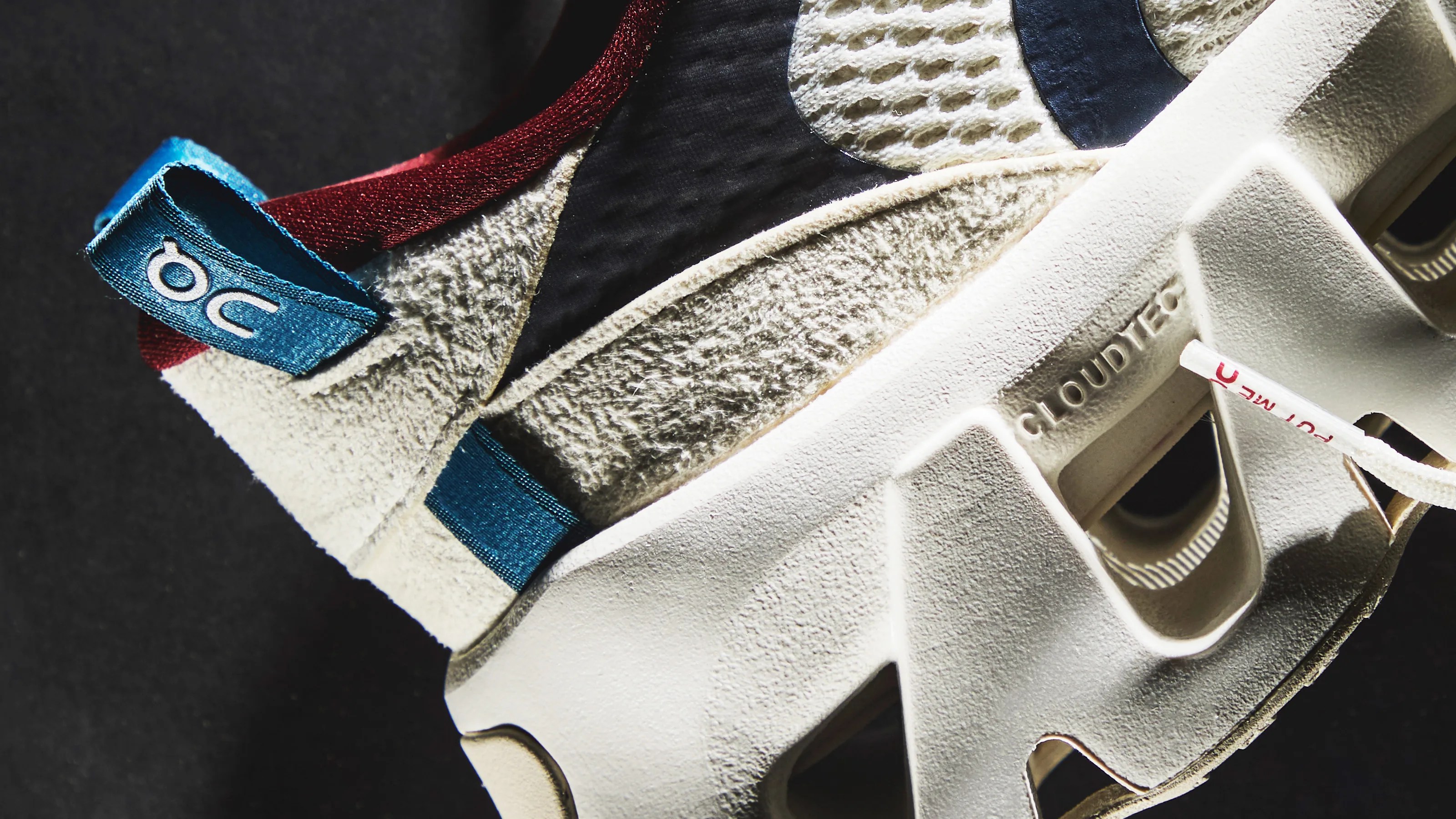 Close-up of a beige sneaker with textured fabric, blue pull tab labeled "OC," and white sole embossed with "CLOUDTEC.
