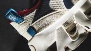 Close-up of a beige sneaker with textured fabric, blue pull tab labeled "OC," and white sole embossed with "CLOUDTEC.