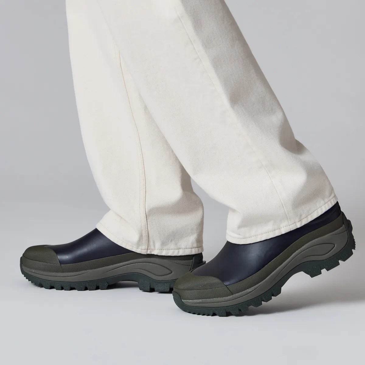 Black and olive green slip-on rubber boots worn with off-white pants.