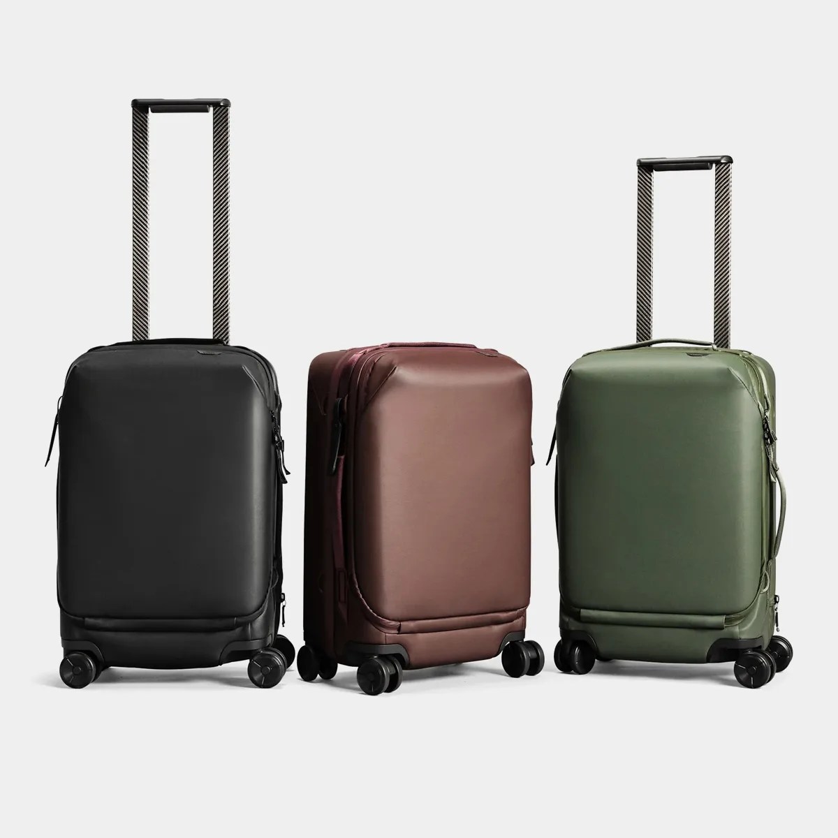 Three upright hard-shell suitcases in black, brown, and olive green with extended telescopic handles and four spinner wheels.
