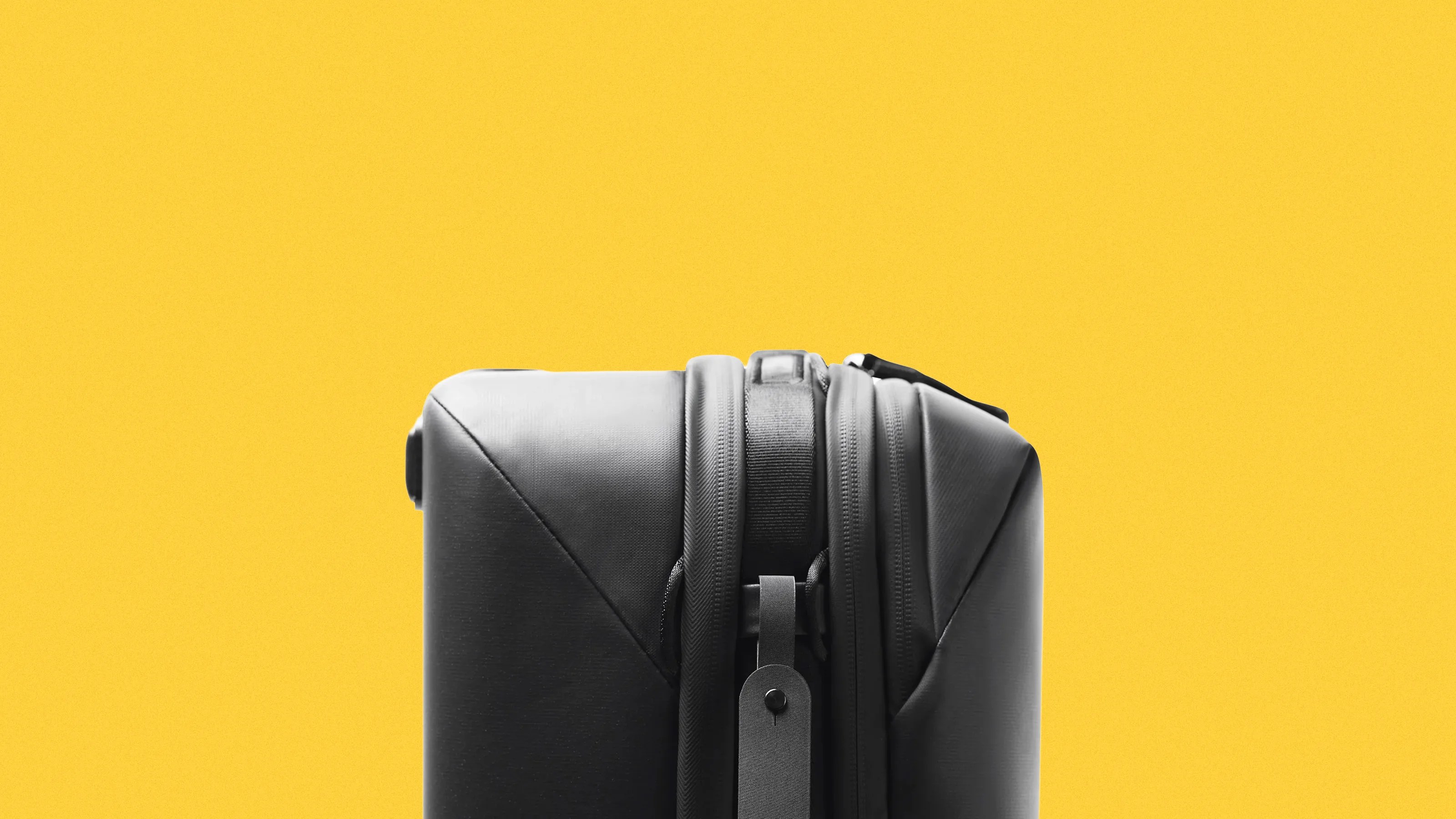 Top view of a black hard-shell suitcase with zippers against a yellow background.