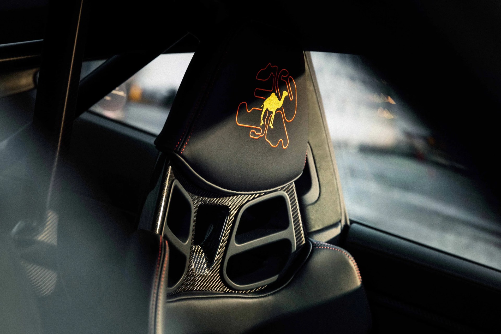 Black leather car seat with red stitching and a yellow camel logo embroidered on the headrest.
