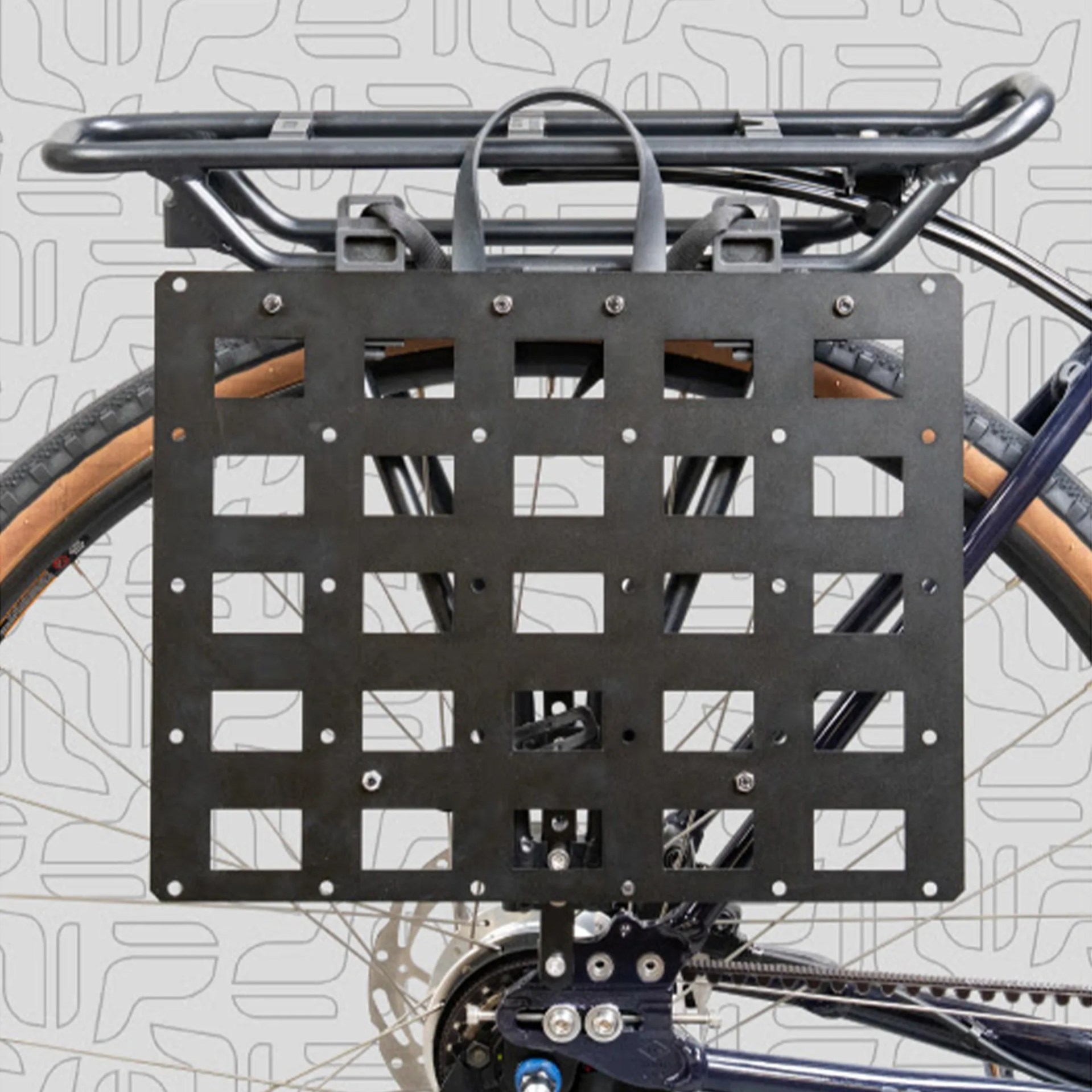 Black metal cargo rack with grid pattern mounted on the rear of a bicycle with tan sidewall tires.