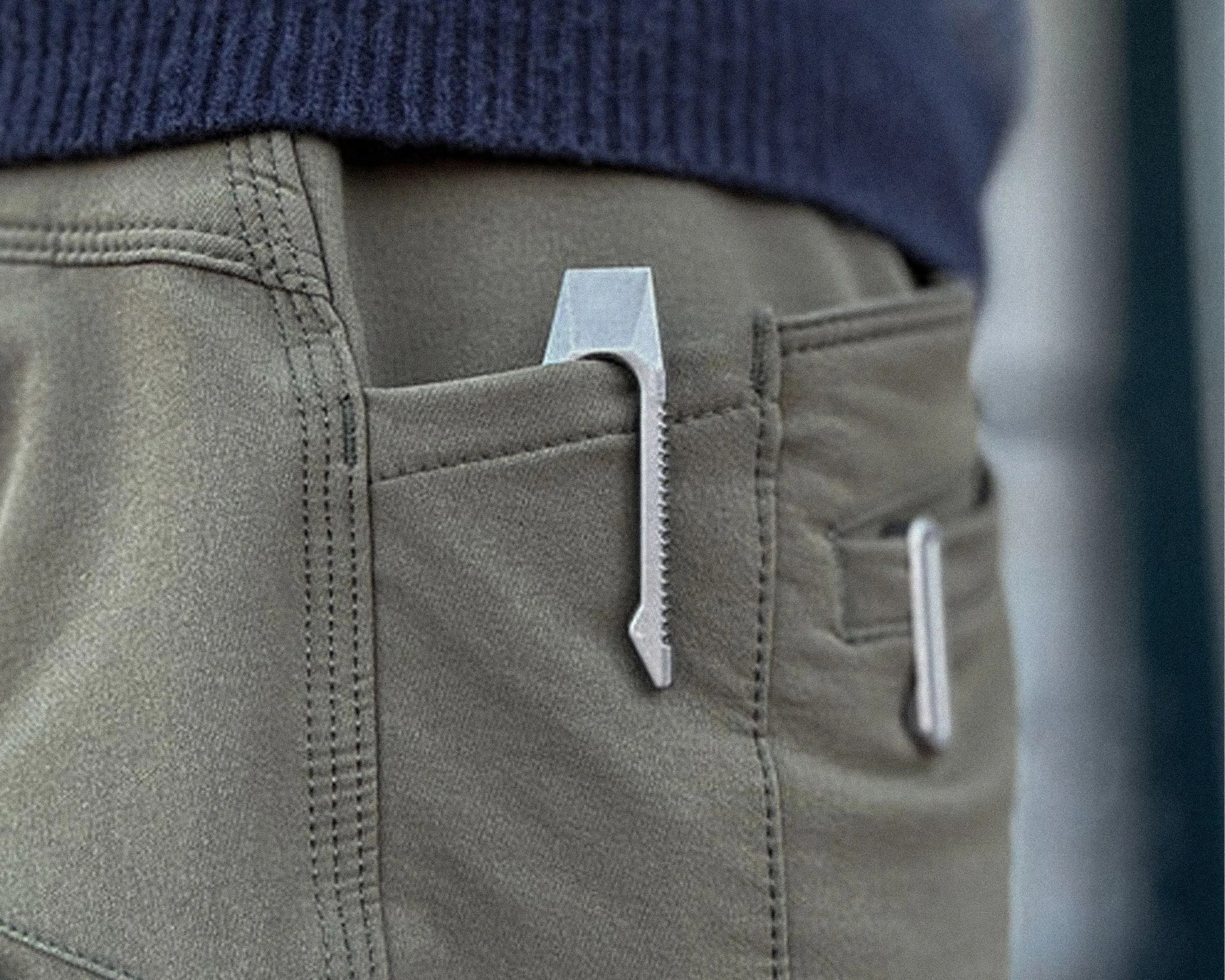 Silver metal clip with serrated edge attached to the pocket of olive green pants.