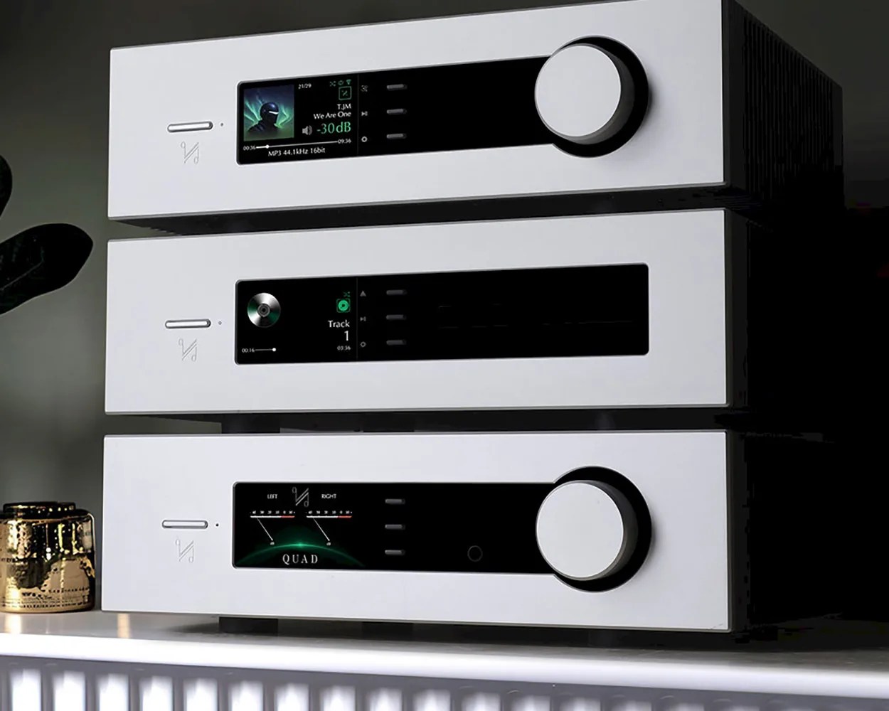 Stack of three white audio components with black display panels and large control knobs on a white surface.