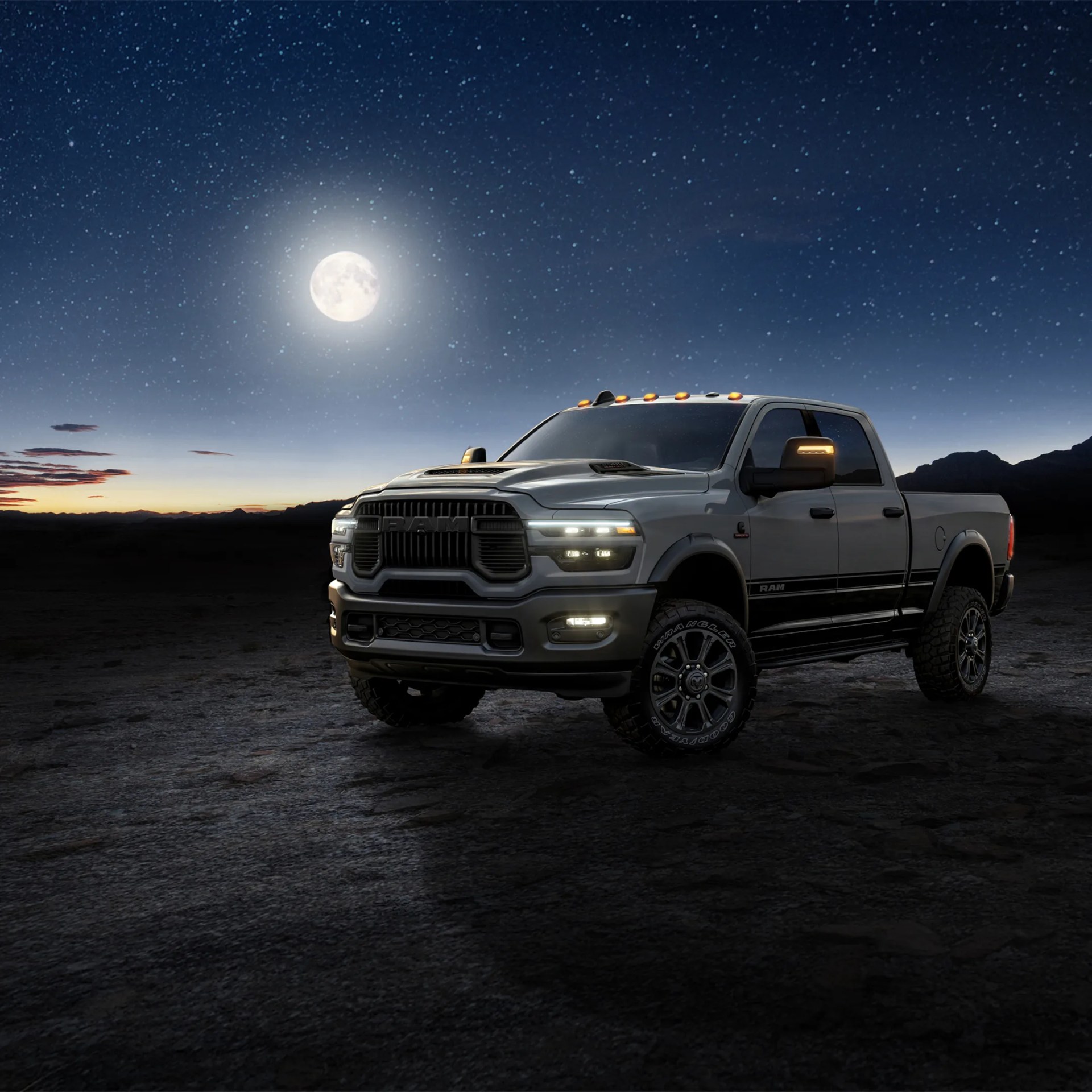 Silver Ram pickup truck with illuminated headlights and roof lights under a starry night sky with a full moon.