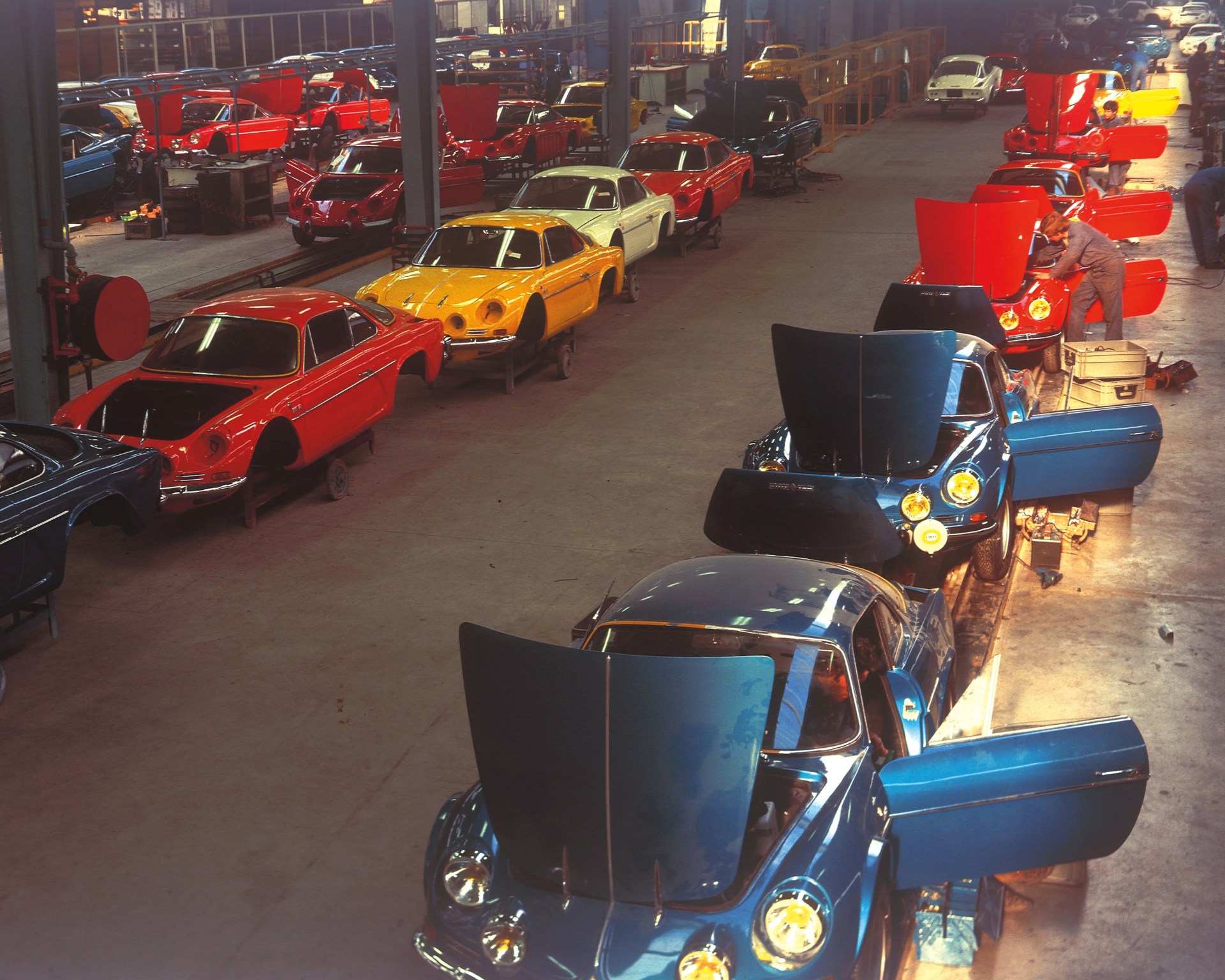 Assembly line of classic sports cars in various colors with open hoods and doors inside a factory.