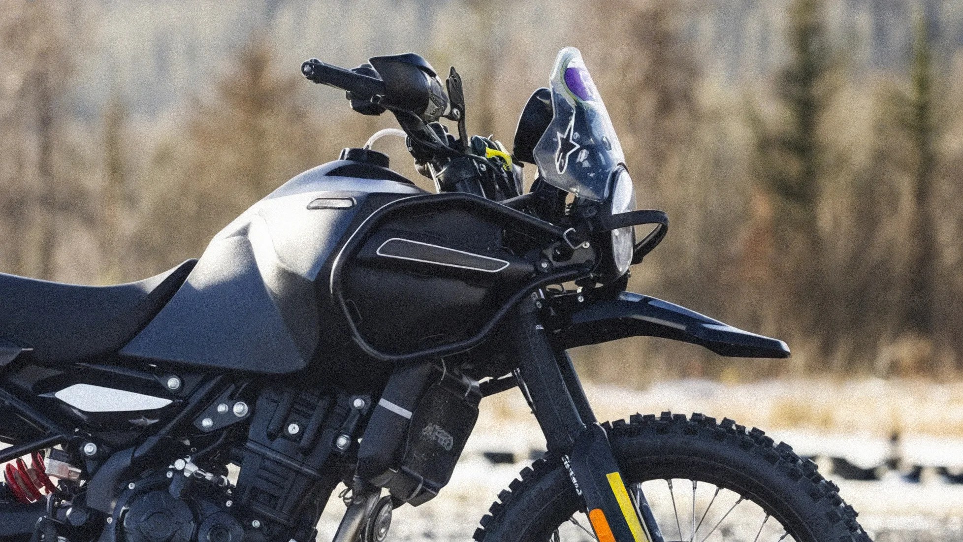 Black adventure motorcycle front with knobby tire, windshield with logo, and protective frame.