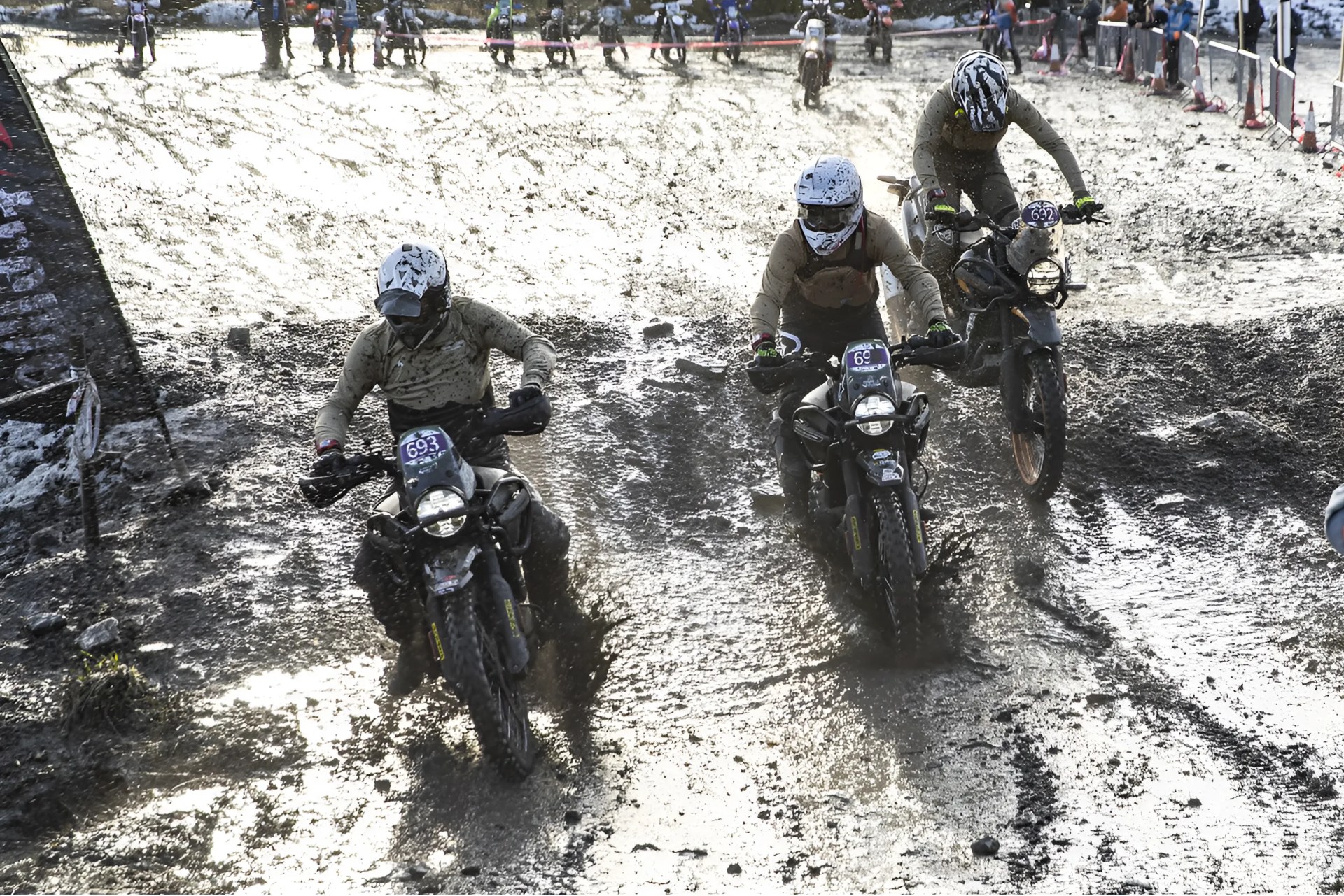 Three motorcyclists wearing helmets riding through muddy terrain during a race.
