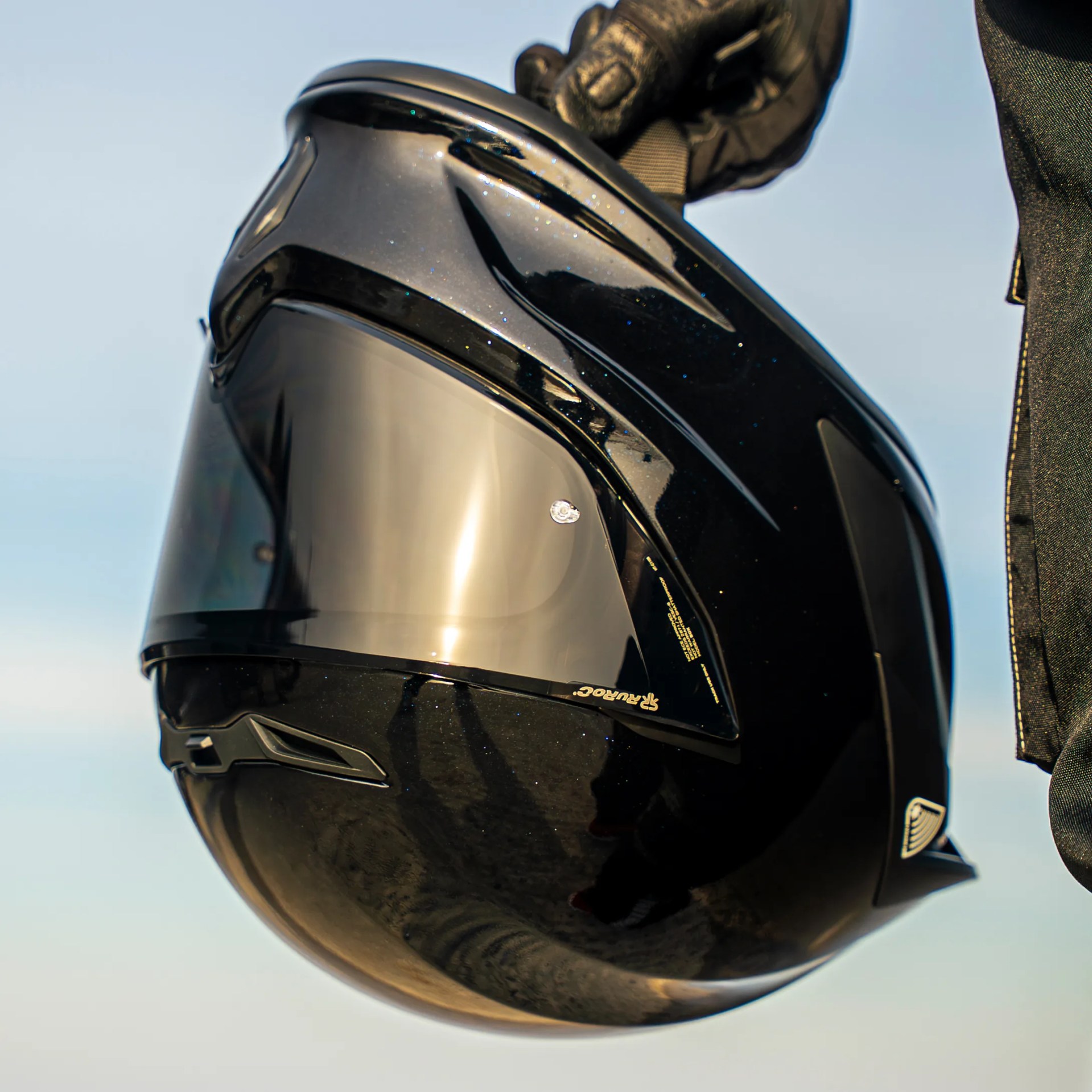 Glossy black full-face motorcycle helmet with tinted visor held by a gloved hand.