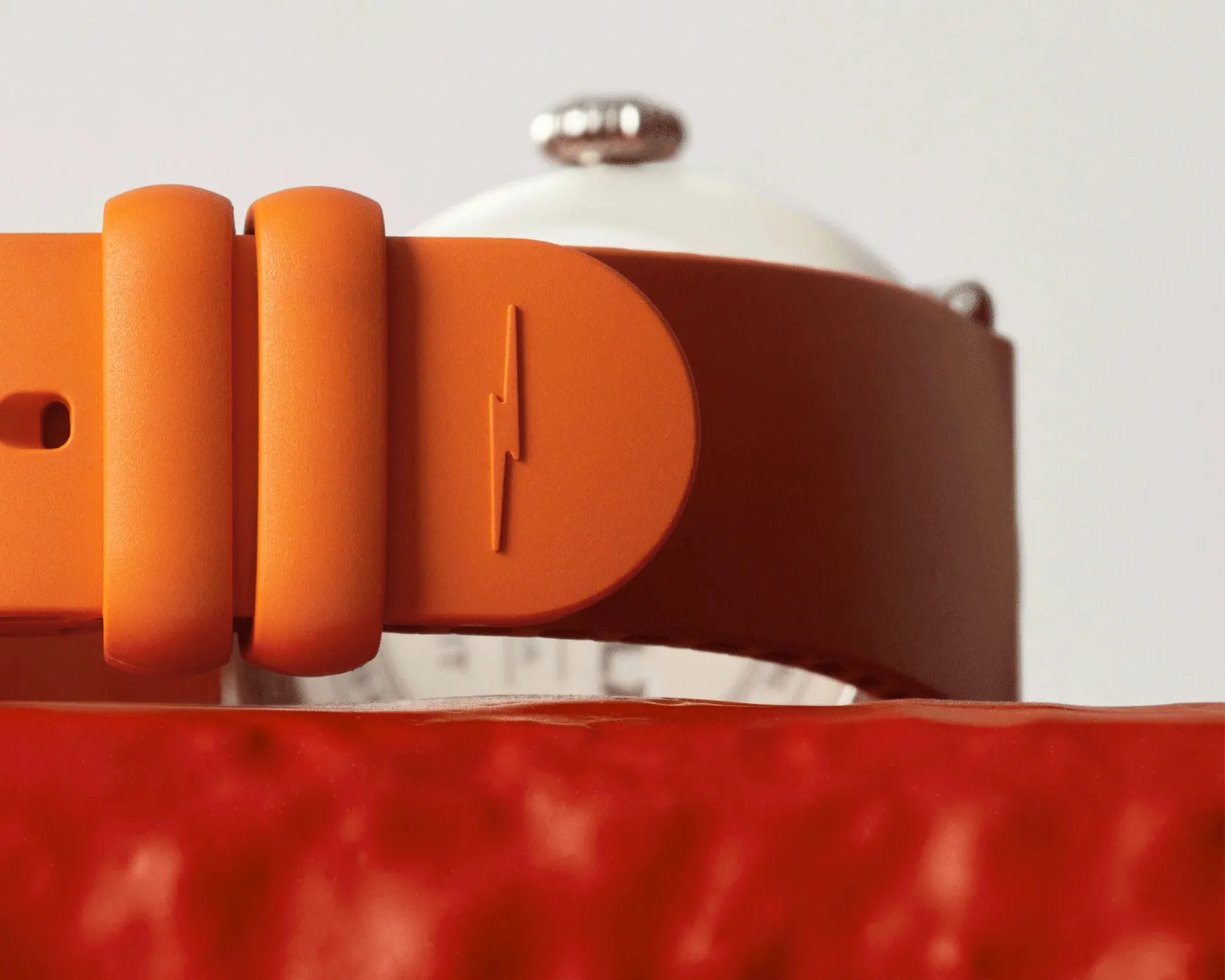 Close-up of an orange silicone watch strap with a lightning bolt symbol, partially showing a white watch face in the background.