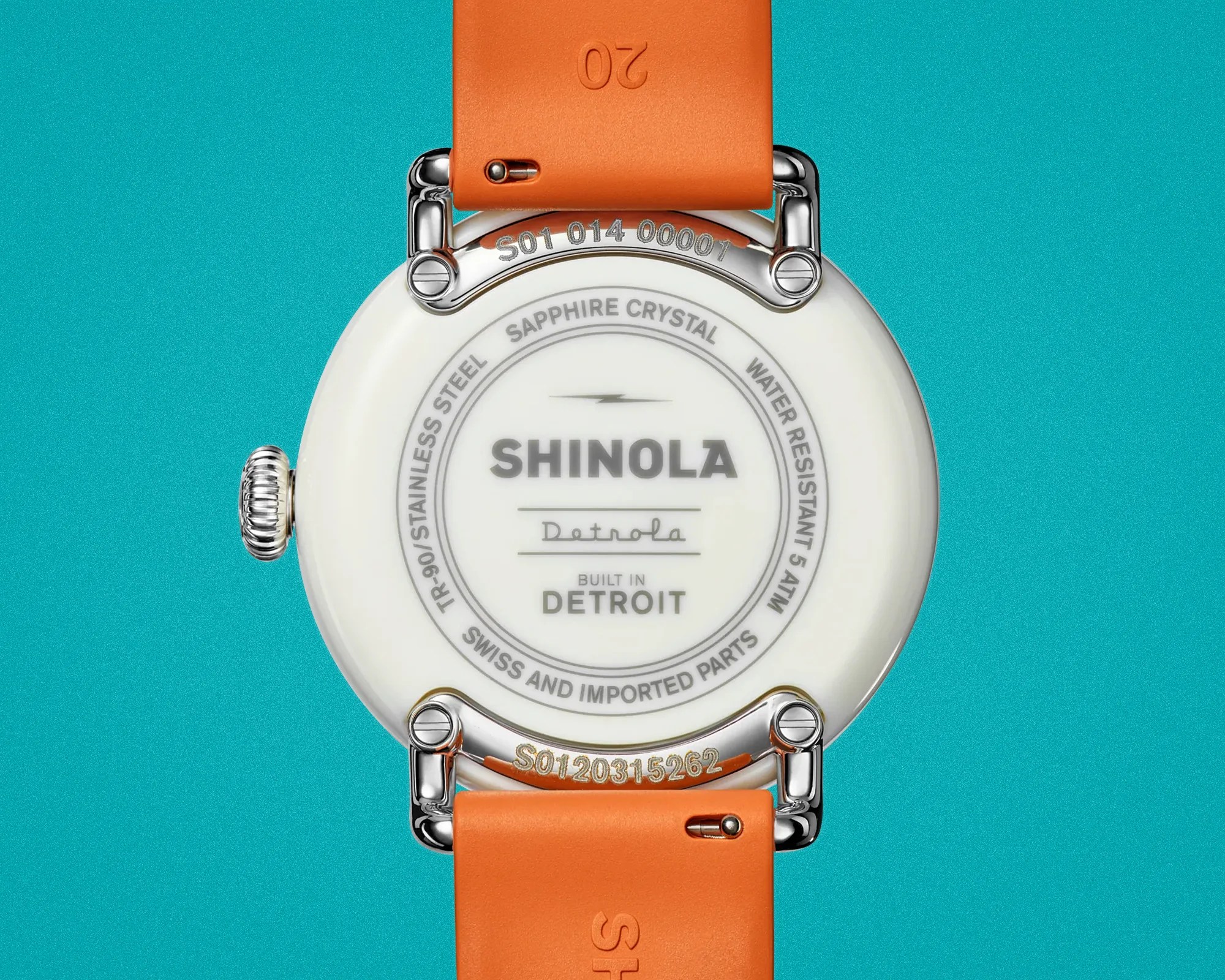 Back of a white Shinola Detrola watch with orange strap on a turquoise background.