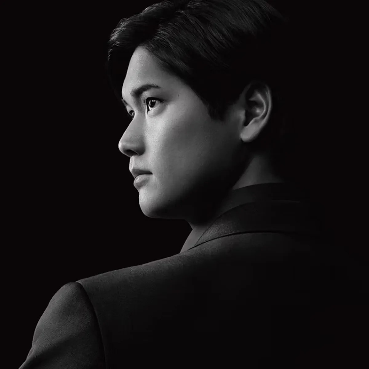Black and white profile portrait of a person wearing a dark suit against a black background.
