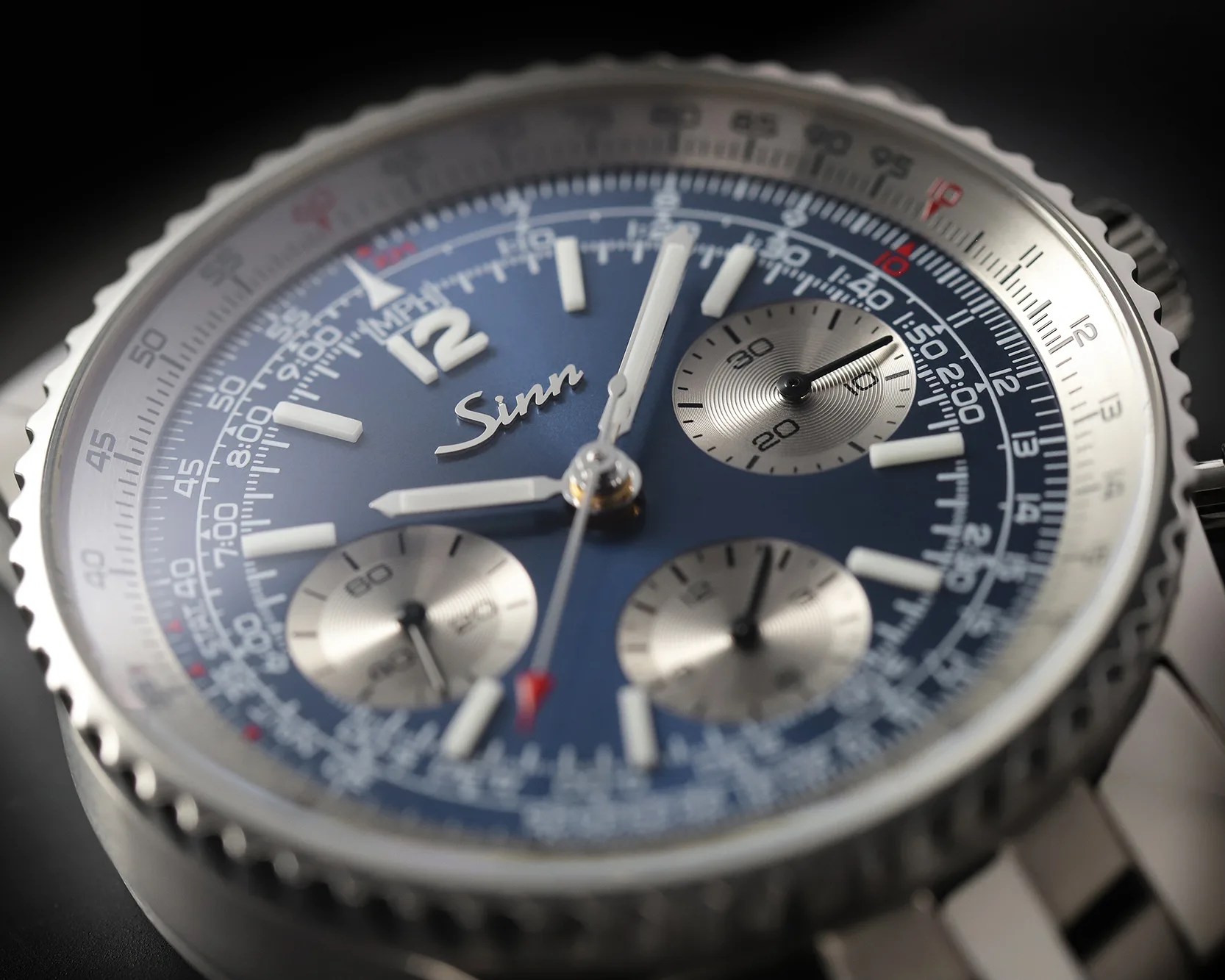 Close-up of a Sinn chronograph watch with a blue dial, three silver subdials, and a stainless steel bezel and bracelet.