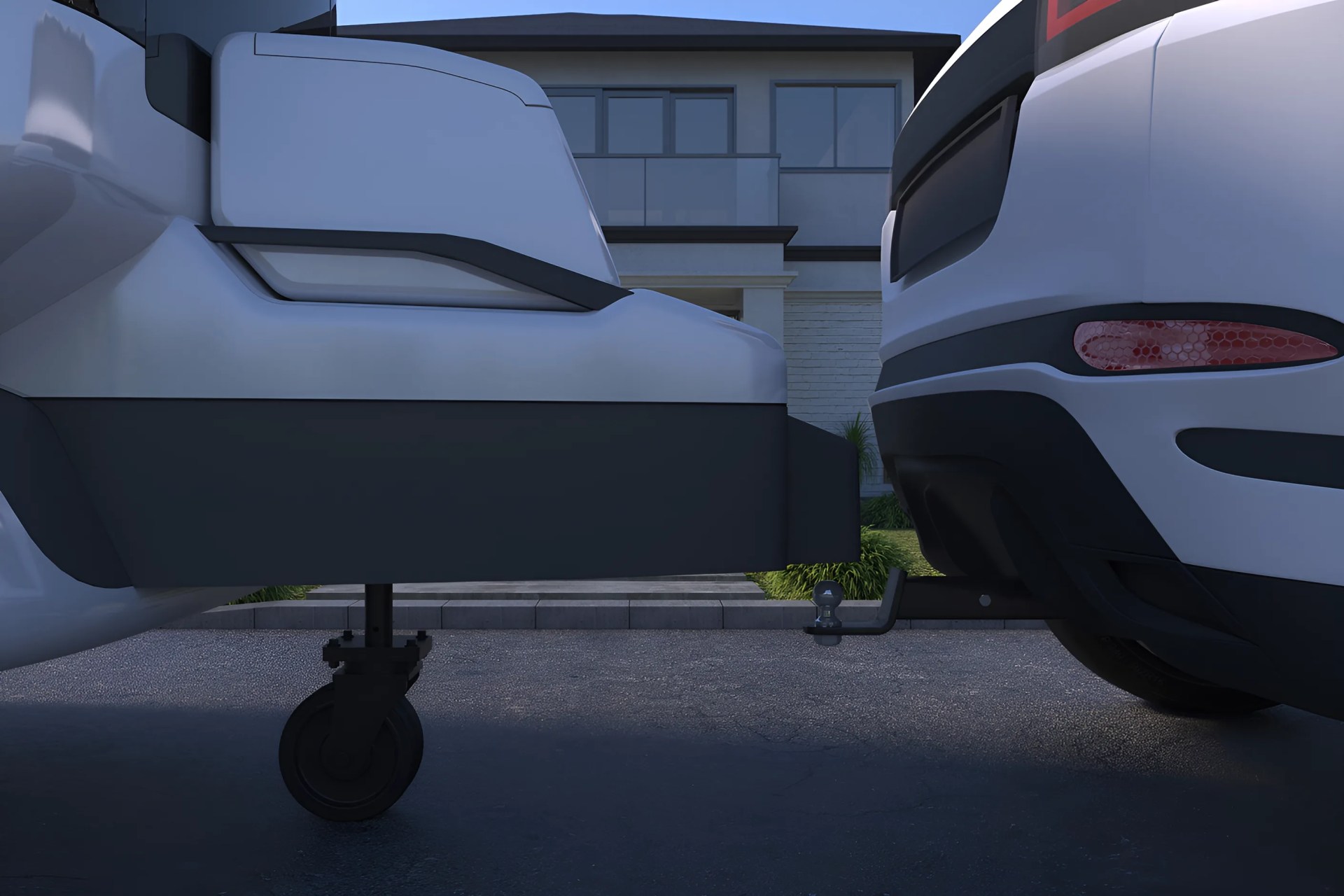 Close-up of a white trailer hitch with a black wheel attached to the rear of a white vehicle in a driveway.