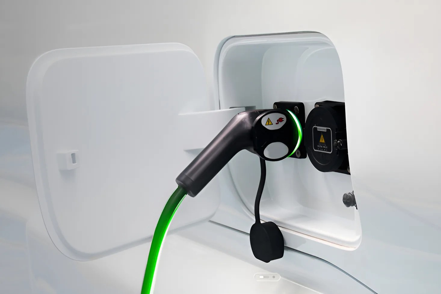 Electric vehicle charging port with a black charging plug and green cable connected to a white car.