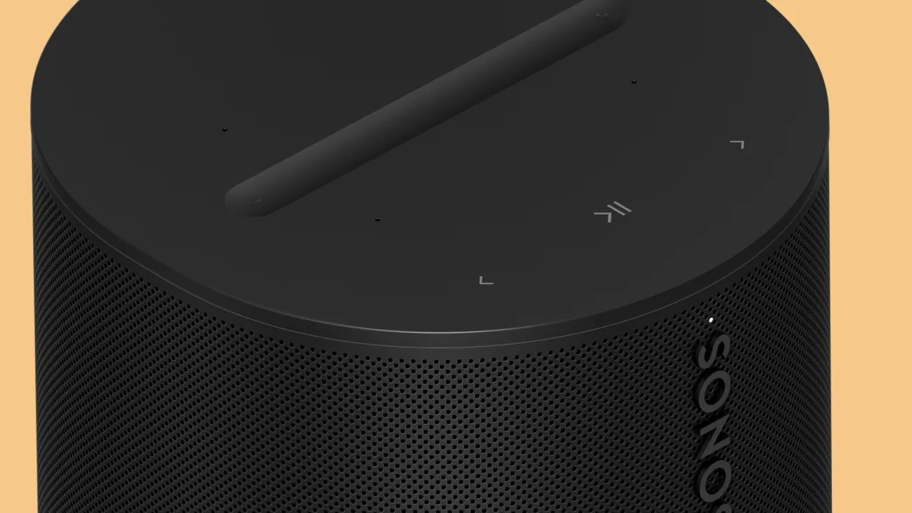 Black cylindrical Sonos speaker with perforated grille and touch controls on top against a beige background.