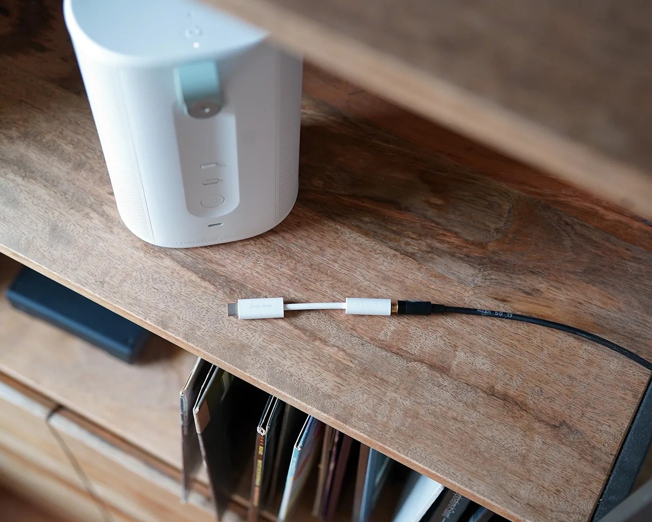 White USB-C to 3.5mm headphone jack adapter cable on a wooden shelf next to a white speaker.
