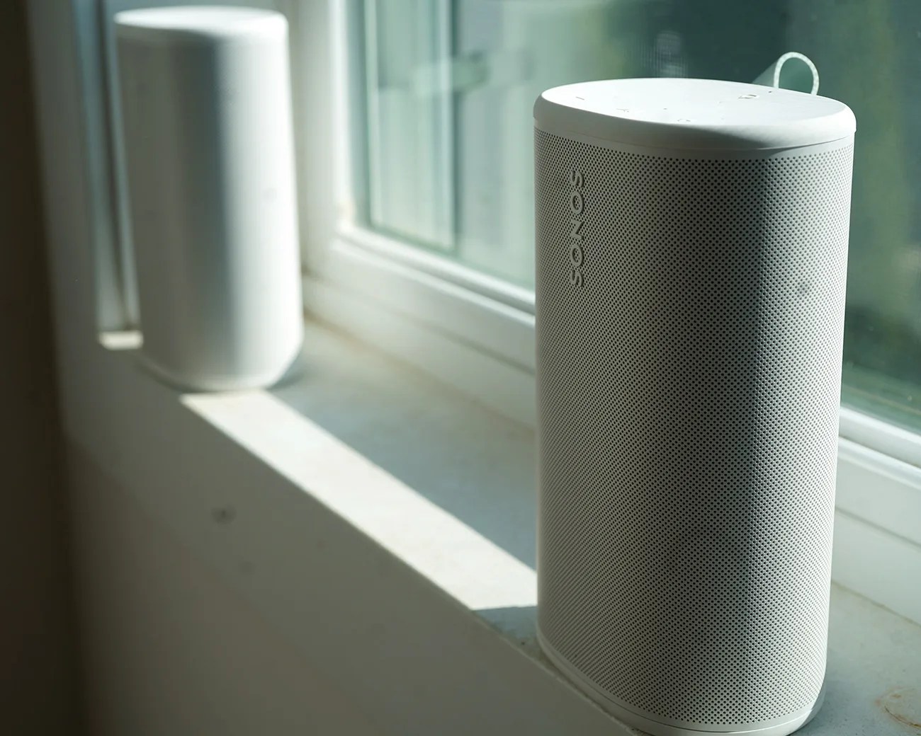 White Sonos speaker on a windowsill with sunlight casting a shadow.