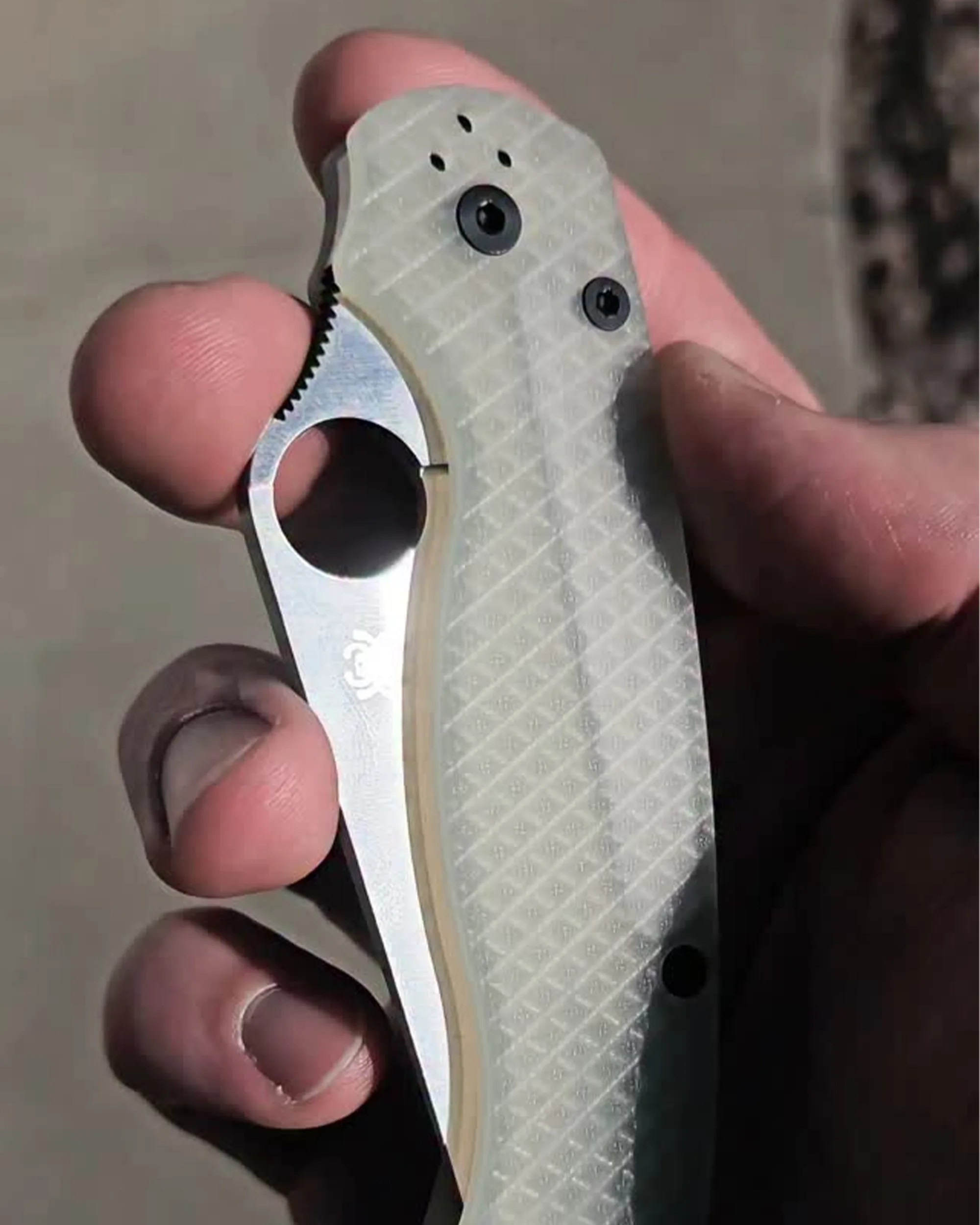 Hand holding a folding knife with a translucent textured handle and partially visible stainless steel blade.