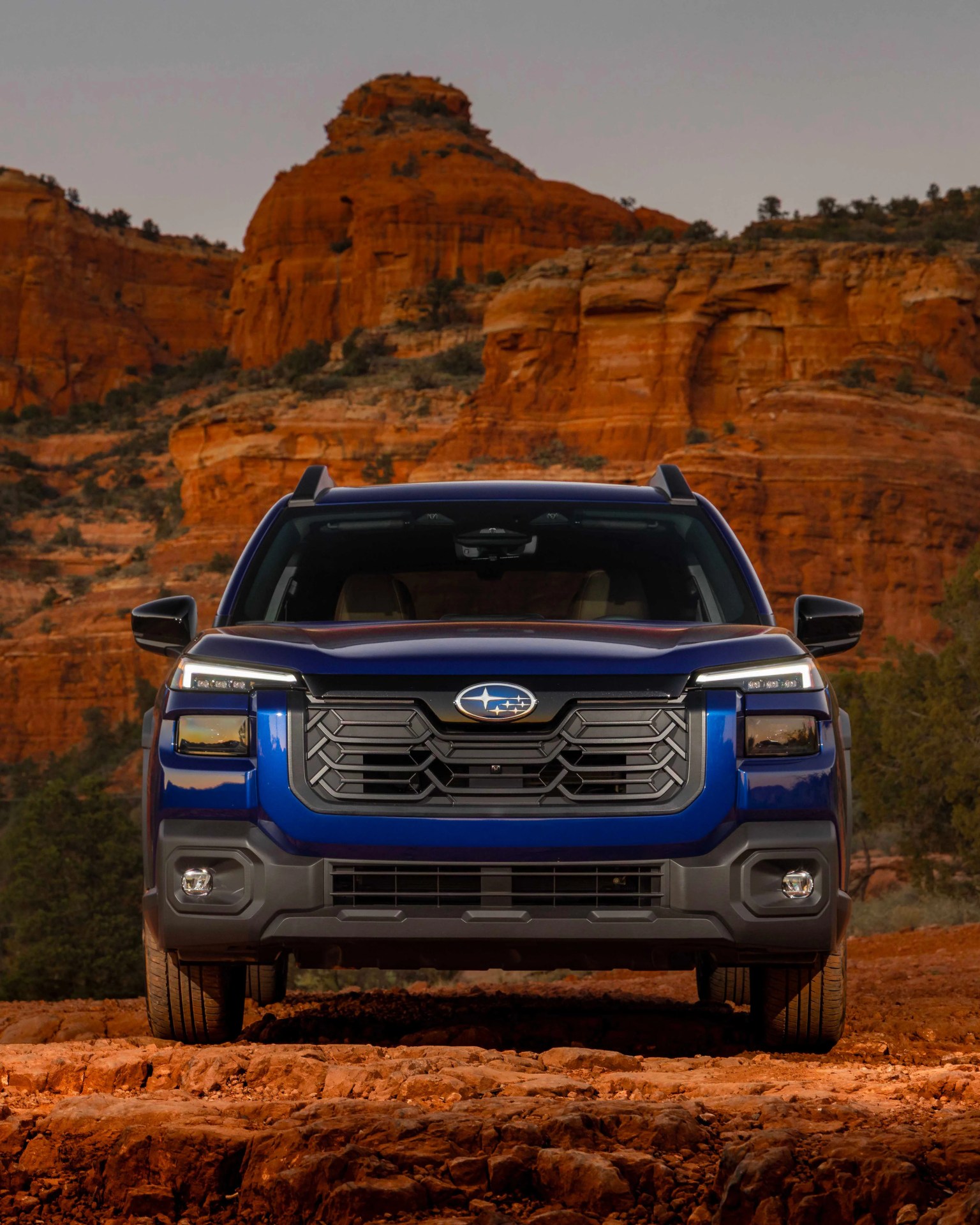 Blue Subaru SUV with black grille parked on rocky red terrain with red rock formations in the background.