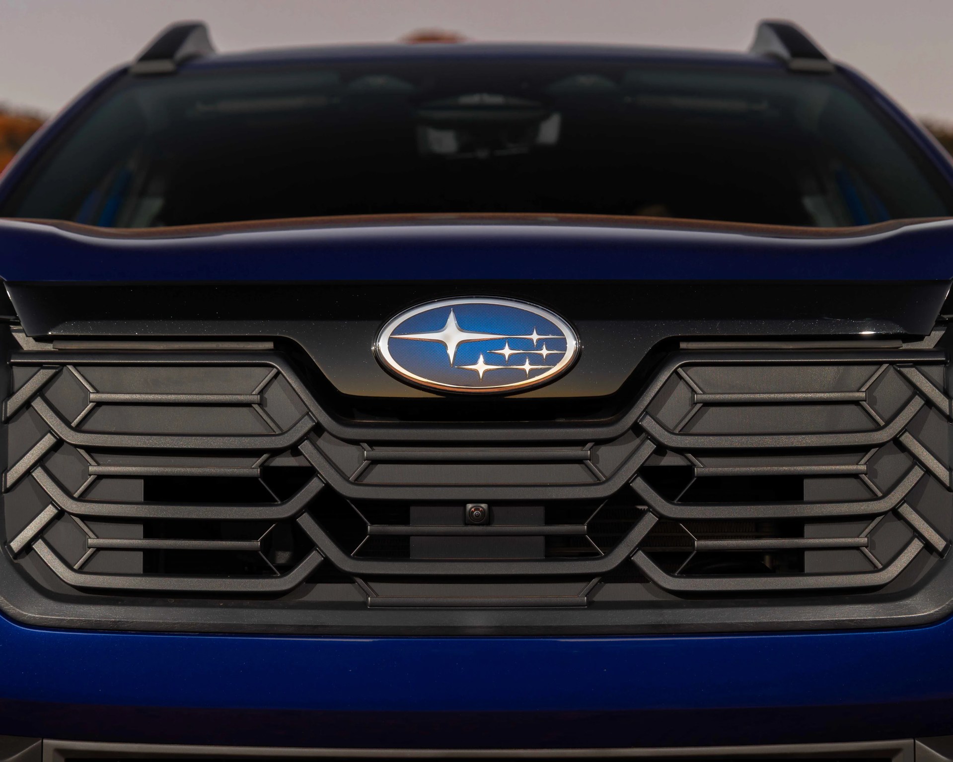 Close-up of a black hexagonal grille with a blue Subaru logo on a dark blue vehicle.
