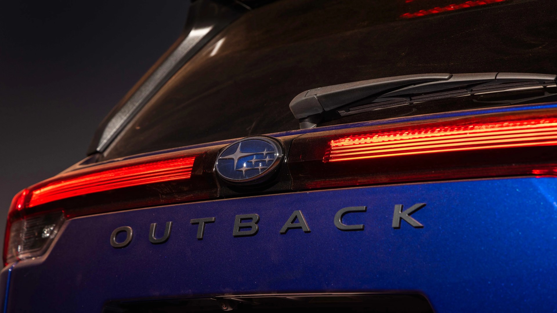 Rear view of a blue Subaru Outback with illuminated red taillights and a rear windshield wiper.