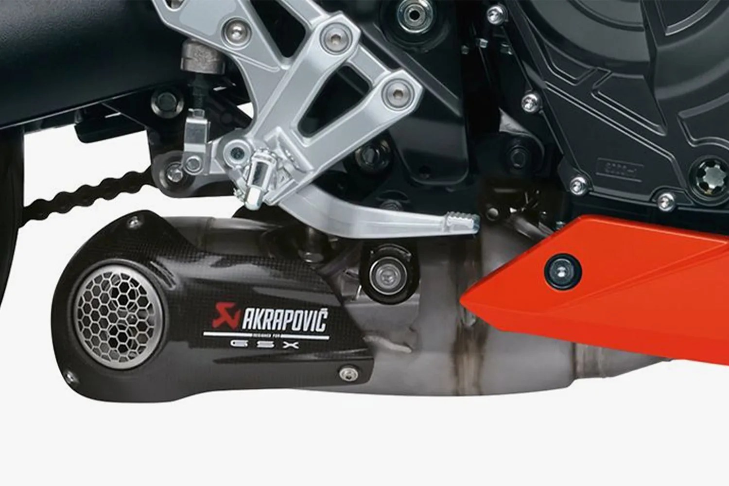 Close-up of a black Akrapovič GSX exhaust system with silver footpeg and red motorcycle fairing.