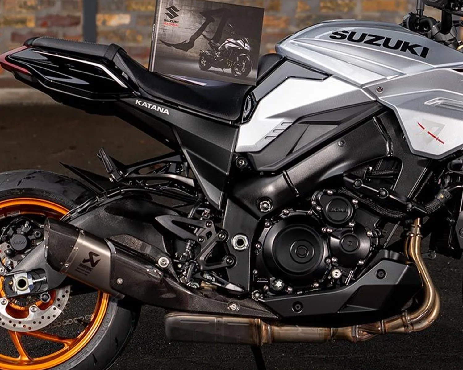 Close-up of a silver and black Suzuki Katana motorcycle with orange rims and an Akrapovič exhaust system.
