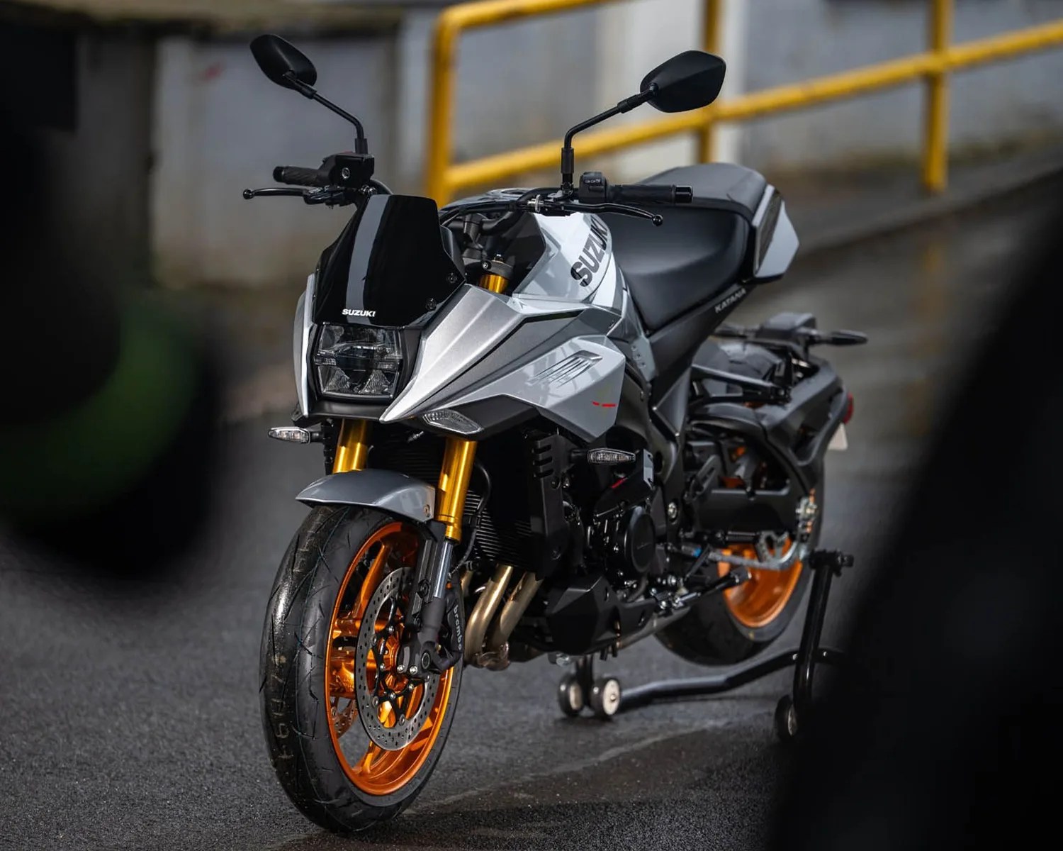 Silver and black Suzuki motorcycle with orange rims on a rear stand on a wet road.