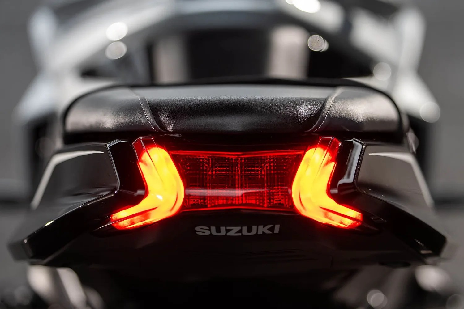 Rear view of a Suzuki motorcycle tail light with illuminated red LED indicators and black leather seat.