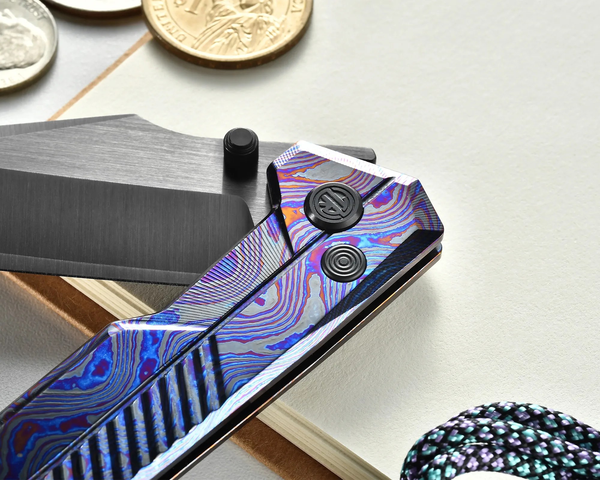 Close-up of a folding knife with a blue and purple patterned handle and a partially open blade on a white surface.