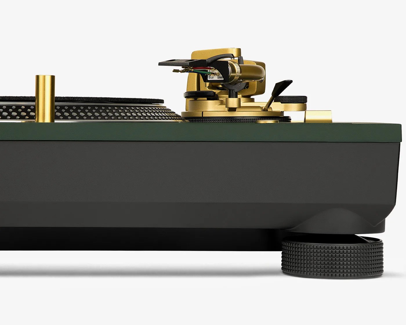 Close-up of a black and green turntable with gold tonearm and black textured feet on a white background.